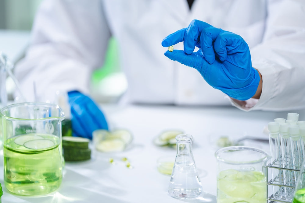 a medicine professional with medical gown and gloves holding a zenutri vitamin oil and on the table the jar filled with liquid for zenutri vitamin formulaation